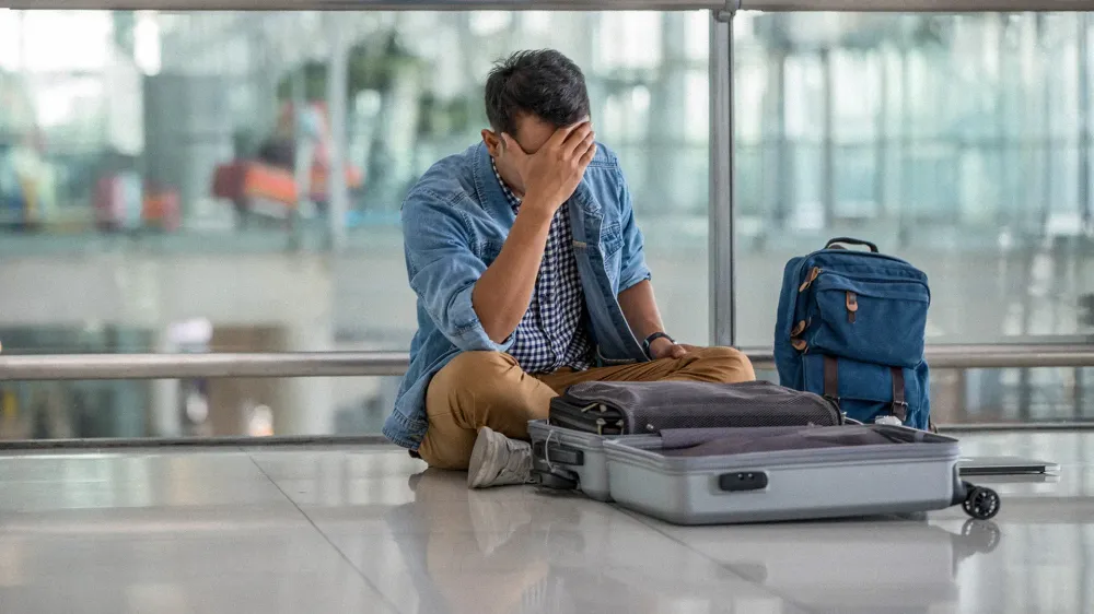man sitting on floor at airport with open luggage lost item